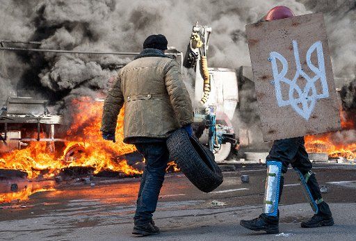 An anti-government protester carrying a tyre walks past a burning vehicle on Sadovaya Street in Central Kiev, Ukraine on February 18, 2014. Photo by Nikita Yurenev\/Itar-Tass\/ABACAPRESS.