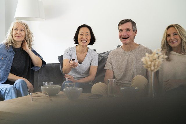 Diverse group of senior friends sitting on sofa watching TV