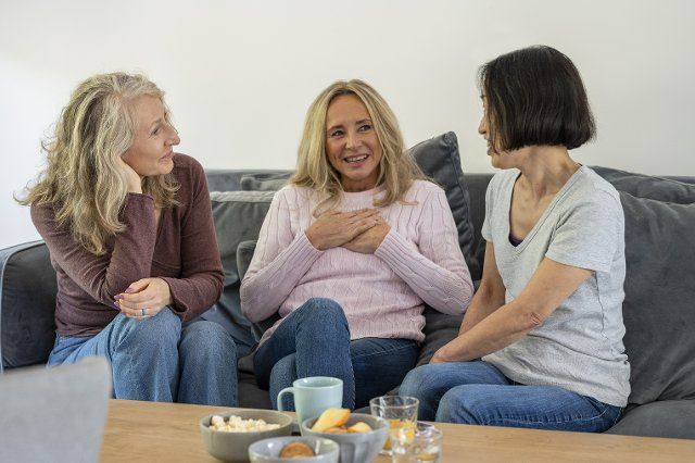 Three senior female friends having a conversation while sitting on sofa at home
