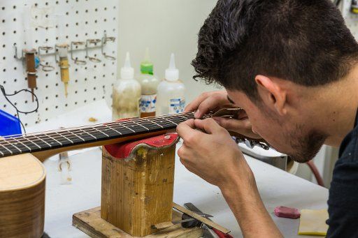 Workers building and assembling guitars at the Taylor Guitar factory in Tecate, Mexico. This worker is adjusting the level of the strings off the guitar neck