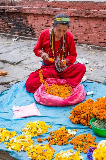 A Nepali woman strings flowers to make garlands for religious offerings at Hindu temples in Kathmandu, Nepal
