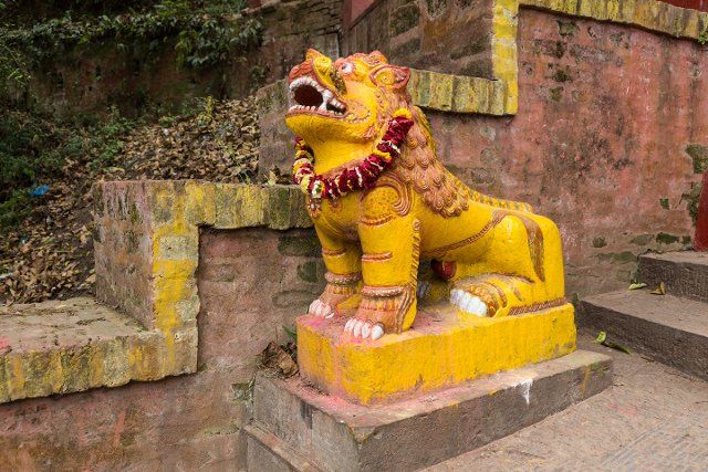 A temple guardian lion with a flower garland at the entrance to the Shesh Narayan Temple, Pharping, Nepal