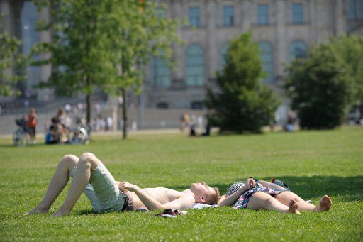 Two tourists bathe in the son on the lawn in front of the Reichstag in Berlin, Germany, 25 July 2012. The weather is predicted to remain sunny and warm with occasional thunderstorms. Photo: MARKUS