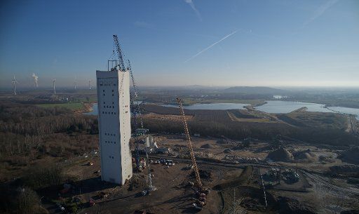 21 January 2020, North Rhine-Westphalia, Kamp-Lintfort: A crane holds a 26-tonne chisel excavator working on the roof of the winding tower of the former Rossenray mine. Starting from the top, the excavator is to demolish the tower, which is over 100 metres high. Photo: Henning Kaiser\/