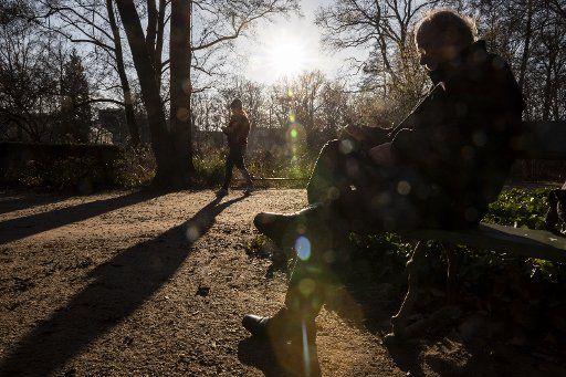 21 January 2020, Berlin: A man sits on a bench in the sunshine in the Tiergarten while a woman walks by. Photo: Christoph Soeder\/