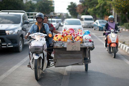 19 October 2019, Thailand, Chiang Mai: A street hawker sits on a motorcycle next to his goods and waits at a traffic light in traffic. Photo: Sebastian Kahnert\/dpa-