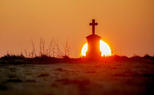 29 December 2019, Baden-Wuerttemberg, Biberach: The sun rises in the morning behind a cross in a field. Photo: Thomas Warnack\/