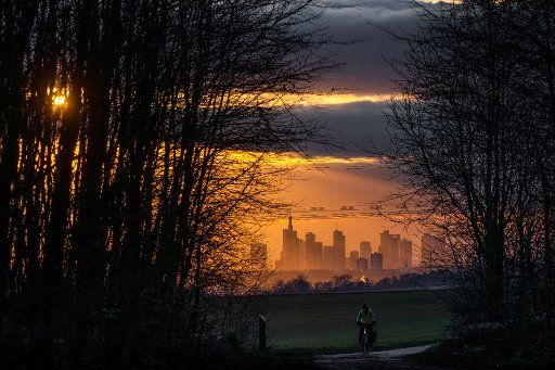 15 January 2020, Hessen, Niederdorfelden: The evening sun shines through the light forest, while in the background the Frankfurt Slyline is visible. Below is a cyclist on the Hohe Straße, a historic trade route that once formed part of the route between the trading cities of Frankfurt am Main and Leipzig. Photo: Frank Rumpenhorst\/