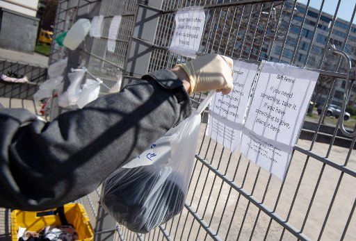 27 March 2020, Baden-Wuerttemberg, Stuttgart: A man hangs a bag on a fence at Marienplatz. The "gift fence" is meant to deposit food, toiletries, clothing, etc. for those in need. Photo: Marijan Murat\/