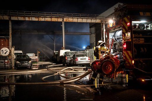 27 March 2020, Bremen: Firefighters are standing in front of a warehouse where a major fire broke out after an explosion. Several vehicles were subsequently set ablaze in a Bremen industrial park. Photo: Sina Schuldt\/