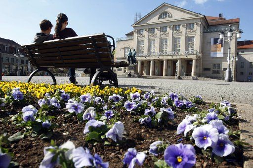 10 April 2020, Thuringia, Weimar: A couple sits on Good Friday in bright sunshine on the pansy-flavoured Theaterplatz in front of the National Theater with the Goethe-Schiller monument. Because of the exit restrictions in connection with the Corona crisis, the square is almost deserted. Photo: Mario Gentzel\/dpa-Zentralbild\/