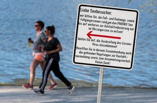 11 April 2020, North Rhine-Westphalia, Dortmund: A sign tells visitors to Lake Phoenix to use the circular route clockwise only to stem the spread of the coronavirus. The artificial lake on the site of a former steelworks is one of the most frequented recreational destinations in the city. Photo: Bernd Thissen\/