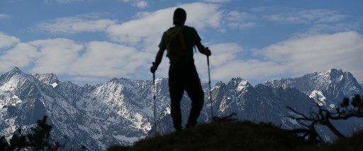 12 April 2020, Bavaria, Garmisch-Partenkirchen: A hiker stands in front of the snow-covered peaks of the Wettersteingebirge, on the left is the triangle of the Alpspitze and on the right the Zugspitze. Photo: Angelika Warmuth\/