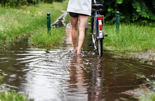 26 June 2020, Berlin: After heavy rain showers, a cyclist pushes her bike through a large puddle. Photo: Jens Kalaene\/dpa-Zentralbild