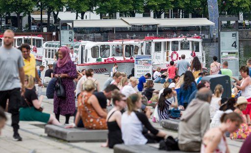 27 June 2020, Hamburg: Passers-by sit in the city centre at the Alster jetty Jungfernstieg in summer temperatures. Photo: Markus Scholz