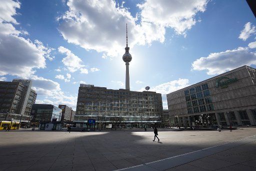26 April 2020, Berlin: The television tower casts a huge shadow on Alexanderplatz, while a single person walks across the large square. Photo: Jörg Carstensen\/