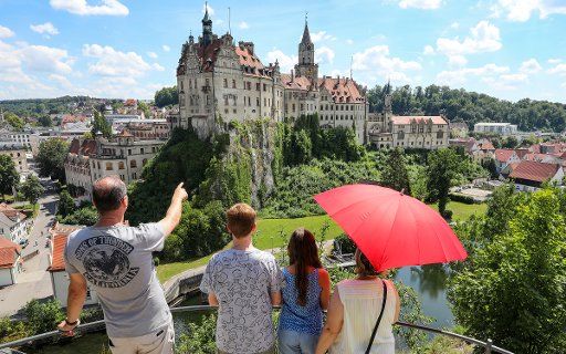 19 July 2020, Baden-Wuerttemberg, Sigmaringen: A family with a parasol in their hands is standing on a viewing platform opposite Sigmaringen Castle. Photo: Thomas Warnack
