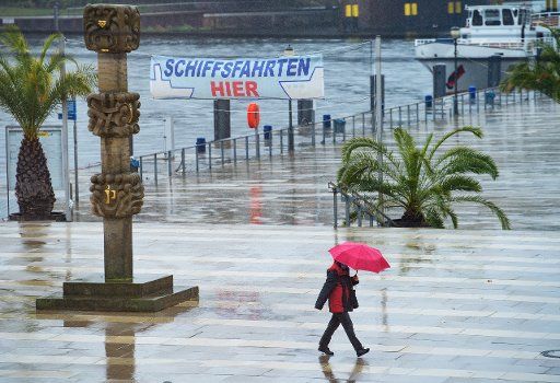 30 October 2020, Brandenburg, Potsdam: A woman walks in pouring rain under a red umbrella in front of the Lange Brücke landing stage past palm trees. Photo: Soeren Stache\/dpa-Zentralbild\/ZB