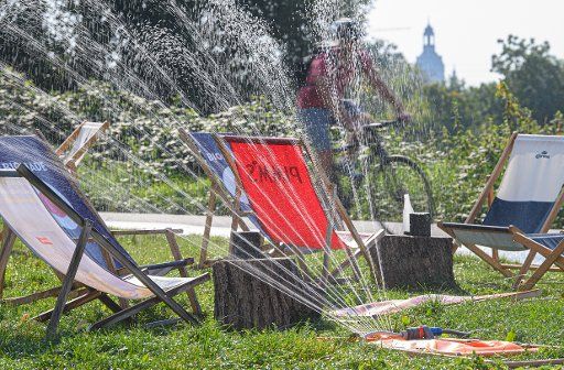 15 September 2020, Saxony, Dresden: A female cyclist rides along the Elbe Cycle Path past a lawn sprinkler and deckchairs on the Citybeach. Photo: Robert Michael\/dpa-Zentralbild\/dpa