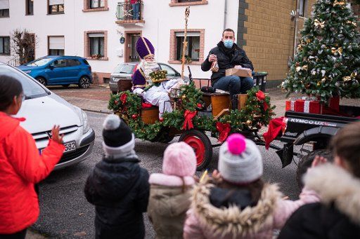 05 December 2020, Saarland, St. Nikolaus: St. Nicholas gives presents to children standing at the roadside while he is pulled through St. Nicholas in a carriage. There is an official St. Nicholas post office in this town in the Saarland. Photo: Oliver Dietze\/dpa