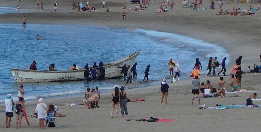 10 December 2020, Spain, Los Cristianos: Refugees land in an open boat on the beach between sunbathing tourists. Photo: Andreas Jütte\/dpa