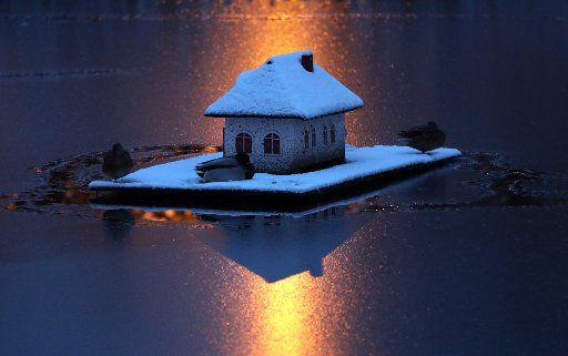 29 December 2020, Mecklenburg-Western Pomerania, Bistow: The floating duck house on the village pond is "sugared" by snow in the early morning, while the light of a street lamp creates a colour mood like sunrise. Temperatures around freezing point and a thin blanket of snow give the north wintry impressions. Photo: Bernd Wüstneck\/dpa-Zentralbild\/dpa