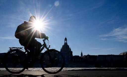 31 December 2020, Saxony, Dresden: A cyclist rides along the Elbe cycle path on the Königsufer opposite the old town with the Frauenkirche in the sunshine, on the left and right of the path there is still artificial snow from the last Ski World Cup. Photo: Robert Michael\/dpa-Zentralbild\/dpa