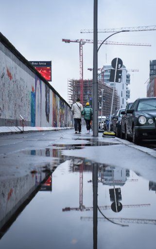 06 January 2021, Berlin: Two people walk along the Berlin Wall in the rain. Photo: Kira Hofmann\/dpa-Zentralbild\/dpa