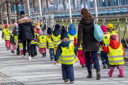 23 February 2021, Bavaria, Munich: Caregivers walk through town with toddlers wearing yellow vests. Photo: Peter Kneffel\/dpa
