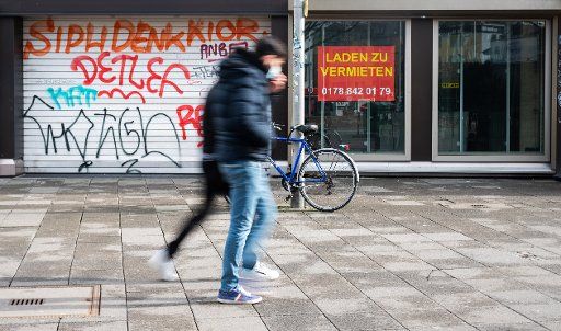 26 February 2021, Lower Saxony, Hanover: Two men walk past two closed storefronts downtown. Photo: Julian Stratenschulte\/dpa