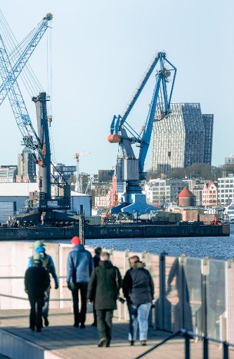 25 December 2020, Hamburg: Walkers walk on the Hansahöft flood protection site. In the background cranes of the southwest harbour and the dancing towers of the Reeperbahn. Photo: Markus Scholz\/dpa