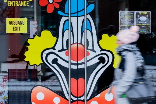 10 February 2021, North Rhine-Westphalia, Duesseldorf: A woman passes an entrance to a closed carnival business adorned by a clown. Carnival is largely cancelled this year due to the Corona Pandemic. Photo: Rolf Vennenbernd\/dpa