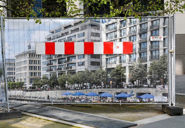 20 April 2021, Berlin: A red and white barrier is attached to a photo with residential and commercial buildings above which the branches of trees can be seen. The poster with the photo serves as a privacy screen on a construction fence. Photo: Jens Kalaene\/dpa-Zentralbild\/ZB