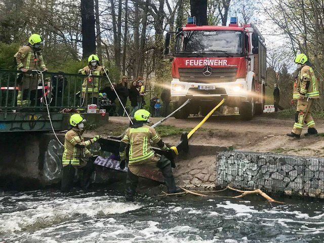 25 April 2021, Berlin: Firefighters fish a bench out of the river Panke. The rescue operation was an interesting spectacle for the parents and their children who were visiting the neighbouring playground. Photo: Jörg Carstensen\/dpa