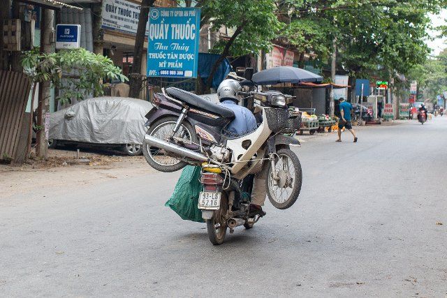 23 April 2021, Vietnam, Hanoi: A rider transports a broken motorcycle on the luggage rack of his bike to Te Lo village. About 1000 families search full-time in about 400 recycling yards for valuable scrap metal to reuse and sell. (to dpa "Graveyard of fire chairs in Vietnam") Photo: Chris Humphrey\/dpa