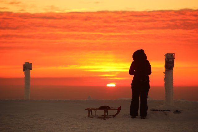 dpatop - 20 March 2021, Saxony-Anhalt, Schierke: A woman with a sledge stands on the Brocken at sunrise. On the highest mountain in the Harz Mountains, the beginning of the calendrical spring was greeted with frosty minus 12 degrees Celsius. Photo: Matthias Bein\/dpa-Zentralbild\/dpa