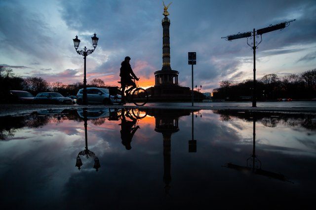 27 March 2021, Berlin: A cyclist rides past the Victory Column at sunset, the scene reflected in a puddle. Photo: Christoph Soeder\/dpa