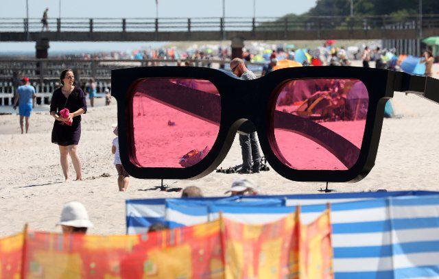 14 June 2021, Mecklenburg-Western Pomerania, Zingst: Holidaymakers enjoy the summer weather on the Baltic Sea beach, a large pair of rose-coloured glasses from the Horizonte photo festival forms a unique backdrop. Photo: Bernd Wüstneck\/dpa-Zentralbild\/dpa