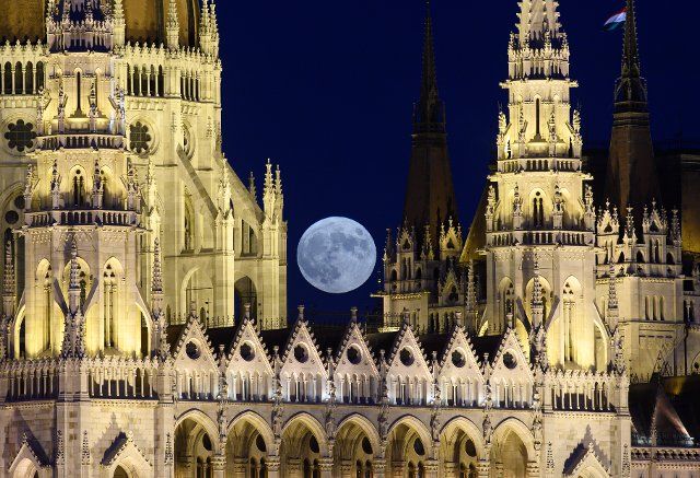 24 June 2021, Hungary, Budapest: The full moon rises over the parliament building on the Danube in the evening. Photo: Robert Michael\/dpa-Zentralbild\/dpa