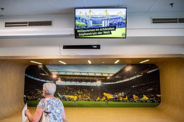 22 July 2021, North Rhine-Westphalia, Dortmund: A woman walks past a monitor with the caption: "Welcome to the most beautiful vaccination centre in the world" and a photo from the stadium at the start of the Corona vaccination campaign at Signal Iduna Park, the home stadium of Bundesliga football team Borussia Dortmund. BVB wants to increase the willingness to be vaccinated - and is enticing everyone who gets vaccinated with a reward. Because those who get vaccinated can take a free walk through the stadium afterwards and take a photo with the DFB trophy. Photo: Guido Kirchner\/dpa