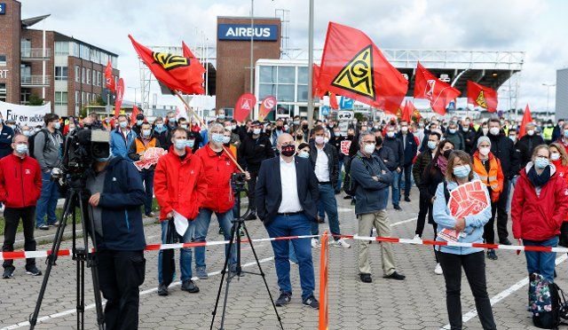 17 September 2021, Hamburg: Employees on warning strike stand with their flags in front of the main entrance of Airbus in Hamburg-Finkenwerder. The IG-Metall trade union is demanding a social collective agreement that regulates the conditions for employees affected by the restructuring. Work stoppages are planned at all affected German sites of Airbus and its subsidiary Premium Aerotec Group. Photo: Markus Scholz\/dpa