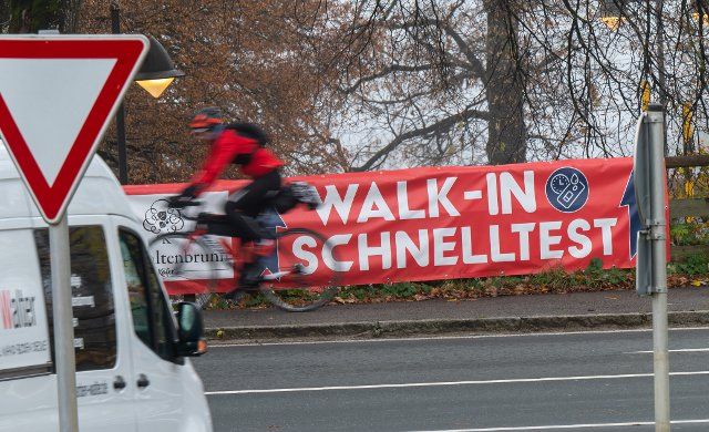 15 November 2021, Bavaria, Gmund Am Tegernsee: A man bicycles past a sign that reads "Walk-In Quick Test" hanging on the side of the road. Photo: Peter Kneffel\/dpa