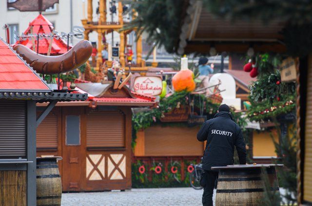 21 November 2021, Saxony, Dresden: A security guard stands in front of closed stalls at the Striezelmarkt on the Altmarkt. Due to Corona, all Christmas markets in Saxony have been cancelled. Photo: Robert Michael\/dpa-Zentralbild\/dpa