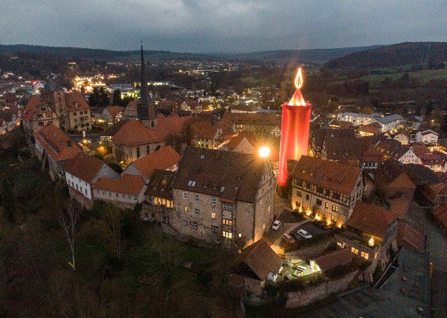29 November 2021, Hessen, Schlitz: The "largest Advent candle in the world" shines above the old town of Schlitz in Hesse. Traditionally, a 35-metre-high tower is covered in red during Advent. Photo: Boris Roessler\/dpa