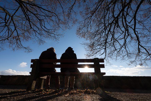 06 December 2021, Hessen, Marburg: A man and a woman sit on a bench under bare branches in the sun. Photo: Sebastian Gollnow\/dpa