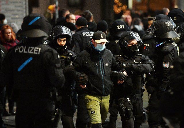 13 December 2021, Thuringia, Erfurt: Police officers lead a man to the personal identification in downtown Erfurt. In Thuringia, hundreds of people protested against the Corona measures at various locations this evening. According to police, about 500 people took part in the protests in Erfurt. Photo: Martin Schutt\/dpa-Zentralbild\/dpa