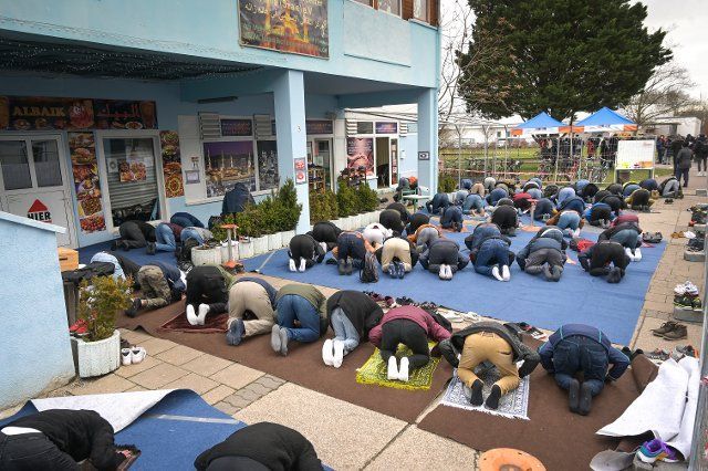 28 January 2022, Saxony-Anhalt, Halle (Saale): Believers kneel at prayer in front of the Islamic Cultural Center in Halle-Neustadt. The Refugee Council of Saxony-Anhalt had called for a solidarity gathering at Friday prayers. The background is renewed shots from an air rifle at an Islamic cultural center in Halle. Photo: Heiko Rebsch\/dpa-Zentralbild\/ZB