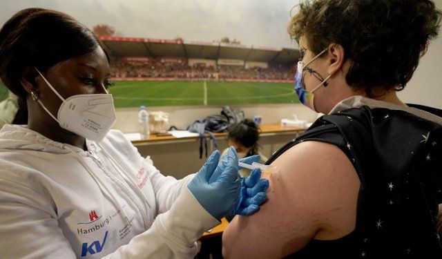 31 January 2022, Hamburg: Selina Bulko (r) receives her booster vaccination during a Corona vaccination campaign at Millerntor Stadium. Until the evening, interested people aged twelve and over can pick up their first, second or booster vaccination in the ballroom of the main stand at Millerntor Stadium. Photo: Marcus Brandt\/dpa