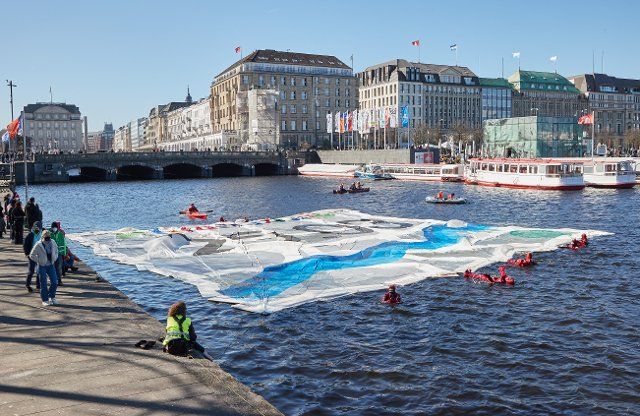 19 March 2022, Hamburg: Activists from the Fridays for Future alliance float a banner with the inscription "Climate strike 25.03." in the Binnenalster lake. Fridays for Future wants to draw attention to the tenth global climate strike with the 400 square meter banner on the Binnenalster. Photo: Georg Wendt\/dpa