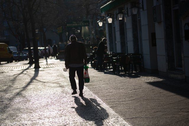 21 March 2022, Berlin: A man walks in the backlight with a mouth-nose protection and a shopping bag in his hands. Photo: Fernando Gutierrez-Juarez\/dpa-Zentralbild\/dpa